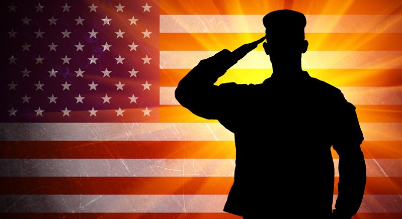A silhouette of a Military Man saluting to the Flag of the American Flag with a burst of light